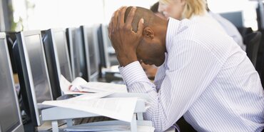 Stressed man in white shirt with head in hands on desk