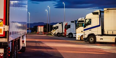 several lorries parked overnight, the sky is an inky blue and the parking is illuminated by street lamps. It's a peaceful image