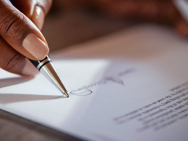 Close up of black hands of businesswoman signing agreement with ballpoint pen. African american hand of a mid adult woman signing a contract. Macro detail of woman signing agreement.