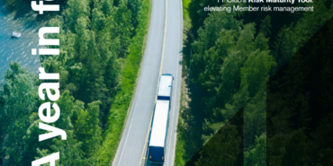 A lorry drives down a bridge with green trees and glistening water ahead. This image is the cover of a publication